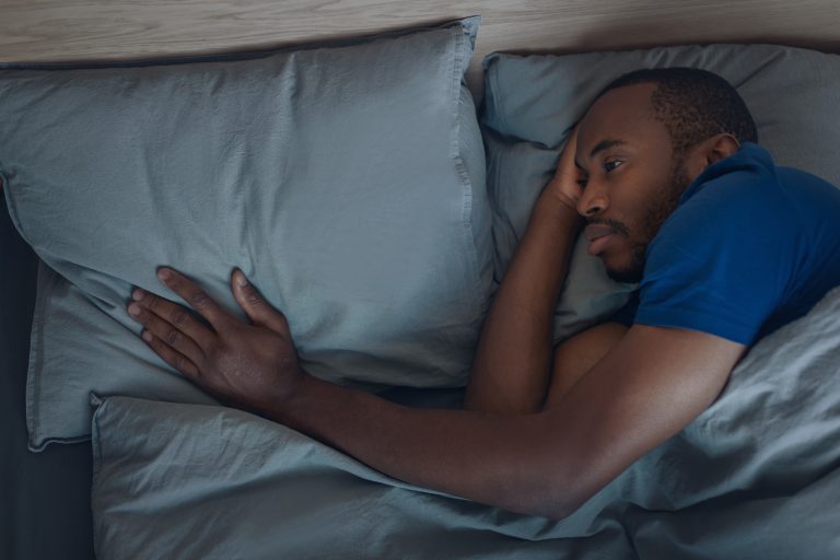 Unhappy Black Man Touching Pillow Lying In Bed Indoor